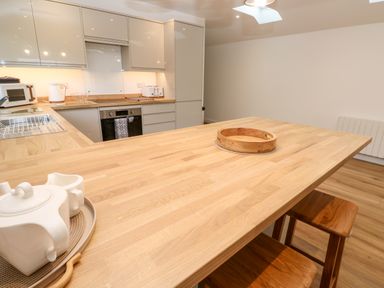 A kitchen with wooden countertops stools and white cabinets at Puffins Rest in Goldsithney