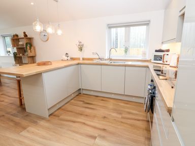 A kitchen with wooden countertops and white cabinets at Puffins Rest in Goldsithney