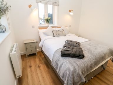 A bedroom with a bed bedside tables and wooden floor at Puffins Rest in Goldsithney