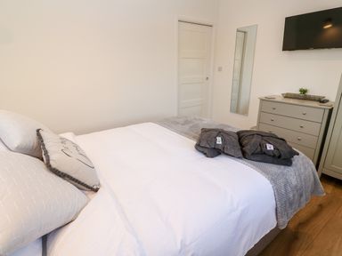 A bedroom with a white bed and grey blankets with a dresser a wall mirror and a television at Puffins Rest in Goldsithney
