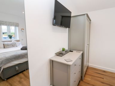 A bedroom with a bed a gray dresser a gray wardrobe and a wall mounted TV at Puffins Rest in Goldsithney