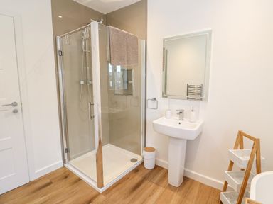 A bathroom with a glass shower enclosure a pedestal sink a mirror and a wooden floor at Puffins Rest in Goldsithney