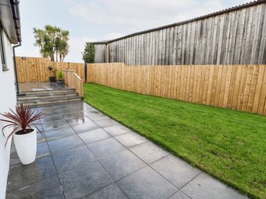 A backyard with tiled patio steps leading to grass and wooden fences at Puffins Rest in Goldsithney