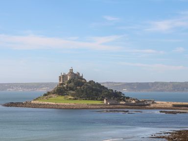 An island with a castle and buildings surrounded by water and hills in the background at Puffins Rest in Goldsithney