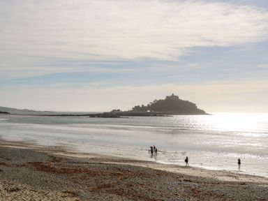 A beach with people walking near the water and a castle on an island in the distance at Puffins Rest in Goldsithney