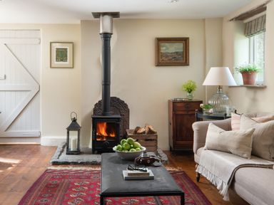 A living room with a wood stove fire a bowl of green apples on a coffee table and a sofa with cushions at Hawthorn Cottage at Collihole in Chagford