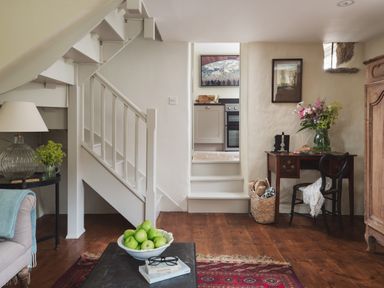 A living room with wooden floor a staircase a small desk with flowers and a chair at Hawthorn Cottage at Collihole in Chagford
