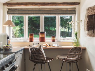 A kitchen counter with two wicker chairs cups pastries and jars by a window at Hawthorn Cottage at Collihole in Chagford