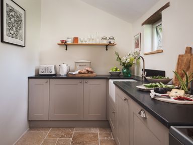 A kitchen with grey cabinets a black countertop a white toaster kettle bread bowl and fruit bowl with flowers at Hawthorn Cottage at Collihole in Chagford