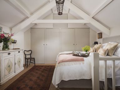 A bedroom with a bed a rug a chair a cabinet and built in closets at Hawthorn Cottage at Collihole in Chagford