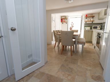 A kitchen with a dining table and chairs a microwave oven and shelves with jars at Belvedere Cottage in Weymouth