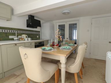 A kitchen with a dining table set for four with beige chairs and green tiled backsplash at Belvedere Cottage in Weymouth