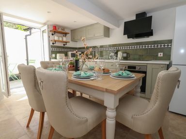A dining table set with plates glasses and napkins in a kitchen with beige chairs and green tiled backsplash at Belvedere Cottage in Weymouth