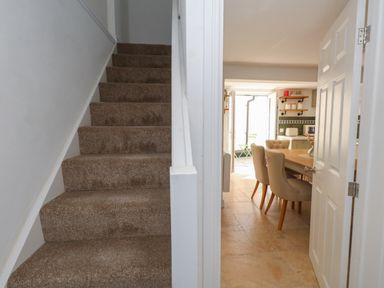 A carpeted staircase next to a dining area with beige chairs and a wooden table at Belvedere Cottage in Weymouth