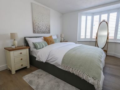 A bedroom with a bed with white and patterned pillows bedside tables with lamps a standing mirror and a painting on the wall at Belvedere Cottage in Weymouth