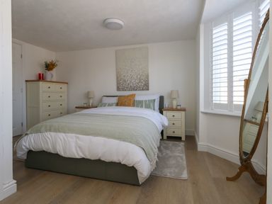 A bedroom with a bed flanked by two nightstands with lamps a dresser and a full length mirror at Belvedere Cottage in Weymouth