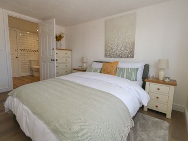 A bedroom with a bed pillows bedside tables lamps and an open door leading to a bathroom at Belvedere Cottage in Weymouth