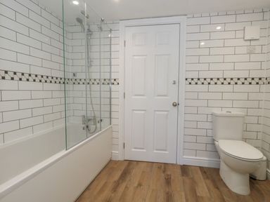 A bathroom with a bathtub shower combination a white door and a toilet at Belvedere Cottage in Weymouth