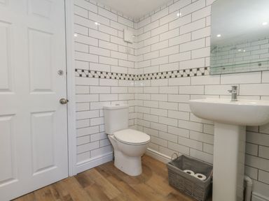 A bathroom with a toilet sink white tiled walls and wood floor at Belvedere Cottage in Weymouth