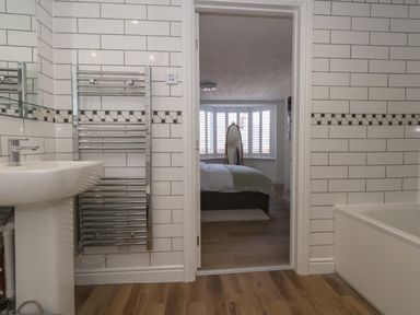 A bathroom with a sink towel radiator and bathtub looking into a bedroom with a bed and a full length mirror at Belvedere Cottage in Weymouth