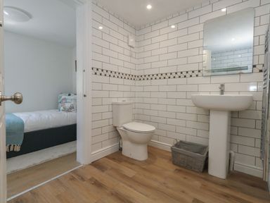 A bathroom with a toilet a pedestal sink a mirror and a basket with a view into a bedroom at Belvedere Cottage in Weymouth