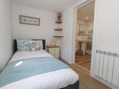 A small bedroom with a single bed a bedside table with lamp and an open door showing a bathroom at Belvedere Cottage in Weymouth