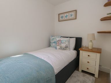 A small bedroom with a single bed and decorative pillows next to a wooden nightstand with a lamp at Belvedere Cottage in Weymouth
