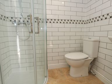 A bathroom with a shower and a toilet with tiled walls at Belvedere Cottage in Weymouth