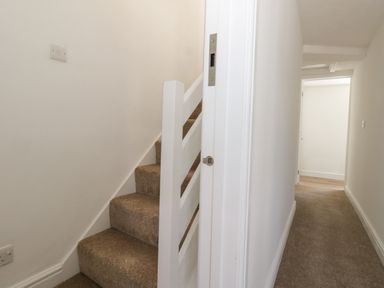 A carpeted staircase next to a carpeted hallway with white walls at Belvedere Cottage in Weymouth