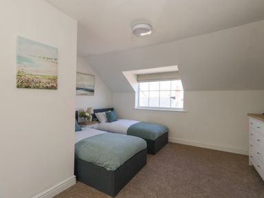 A bedroom with two single beds bedside table with lamp and flowers a window and chest of drawers at Belvedere Cottage in Weymouth