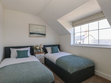 A bedroom with two single beds a bedside table a lamp and a window at Belvedere Cottage in Weymouth