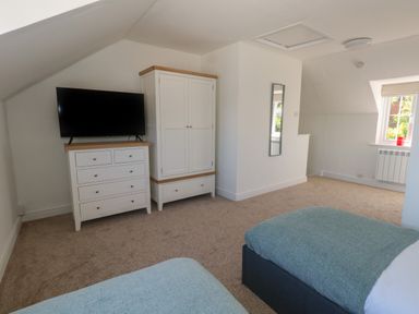 A bedroom with two beds a chest of drawers with a television a wardrobe and a window at Belvedere Cottage in Weymouth