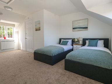 A bedroom with two single beds with teal blankets and pillows and a window on the left at Belvedere Cottage in Weymouth