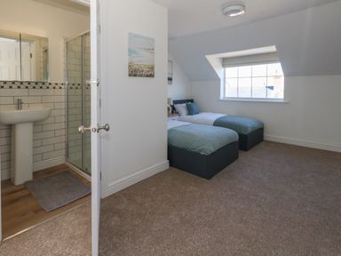 A bedroom with two single beds under a window and an open door leading to a bathroom with a sink and shower at Belvedere Cottage in Weymouth