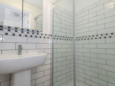A bathroom with a white pedestal sink and a glass shower enclosure with tiled walls at Belvedere Cottage in Weymouth