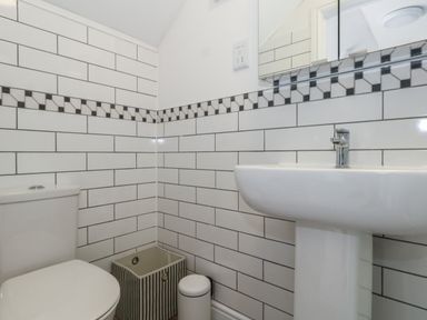 A bathroom with a toilet a pedestal sink a striped basket and a small trash can at Belvedere Cottage in Weymouth