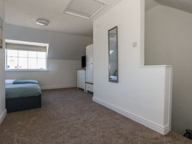 A bedroom with two beds a window carpeted floor a dresser wardrobe a wall mirror and a small wall partition at Belvedere Cottage in Weymouth