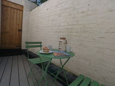 An outdoor seating area with a green metal table and two chairs a wooden door and a white brick wall at Belvedere Cottage in Weymouth