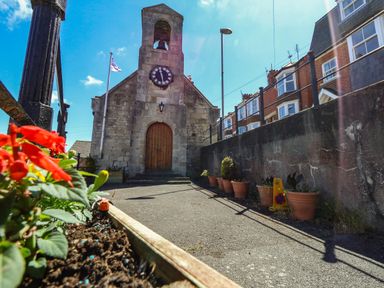 A stone clock tower building with a wooden door and flower pots along a wall in a residential area at Belvedere Cottage in Weymouth