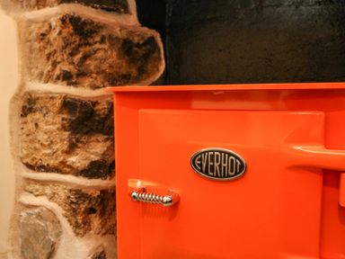 A close up of an orange Everhot stove next to a stone wall at Josie in Pentewan