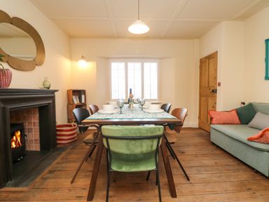 A dining room with a wooden table set with bowls and glasses near a fireplace and a sofa at Josie in Pentewan