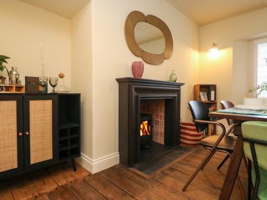 A dining area with a lit fireplace wooden floor a cabinet and a table with chairs at Josie in Pentewan