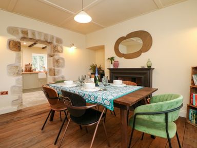 A dining room with a wooden table set for four and an arched stone doorway to a kitchen at Josie in Pentewan