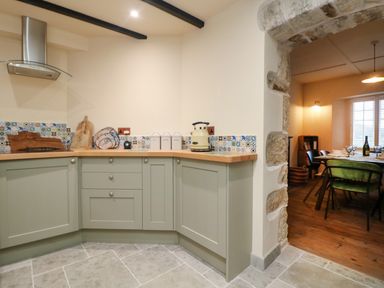A kitchen with green cabinets wooden countertop and a kettle next to a stone archway leading to a dining area at Josie in Pentewan