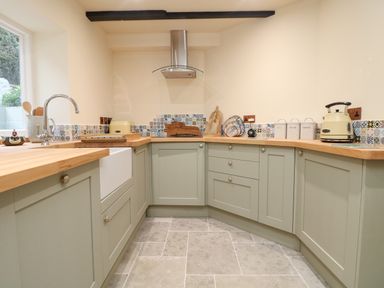 A kitchen with green cabinets wooden countertops mosaic tile backsplash and stainless steel hood at Josie in Pentewan