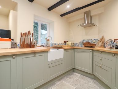 A kitchen with wooden countertops a knife block farm sink and patterned tile backsplash at Josie in Pentewan