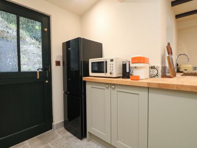 A kitchen corner with a black refrigerator white microwave orange coffee machine knife block and sink at Josie in Pentewan