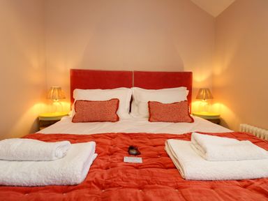 A bedroom with a double bed orange headboard and bedspread side tables with lamps and towels on the bed at Josie in Pentewan