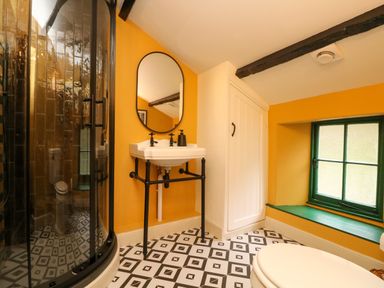 A bathroom with a corner shower unit white sink and mirror a small cabinet and a window with green frame at Josie in Pentewan