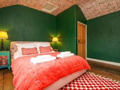 A bedroom with a double bed with orange bedding and pillows two lamps on bedside tables and a wooden door at Josie in Pentewan